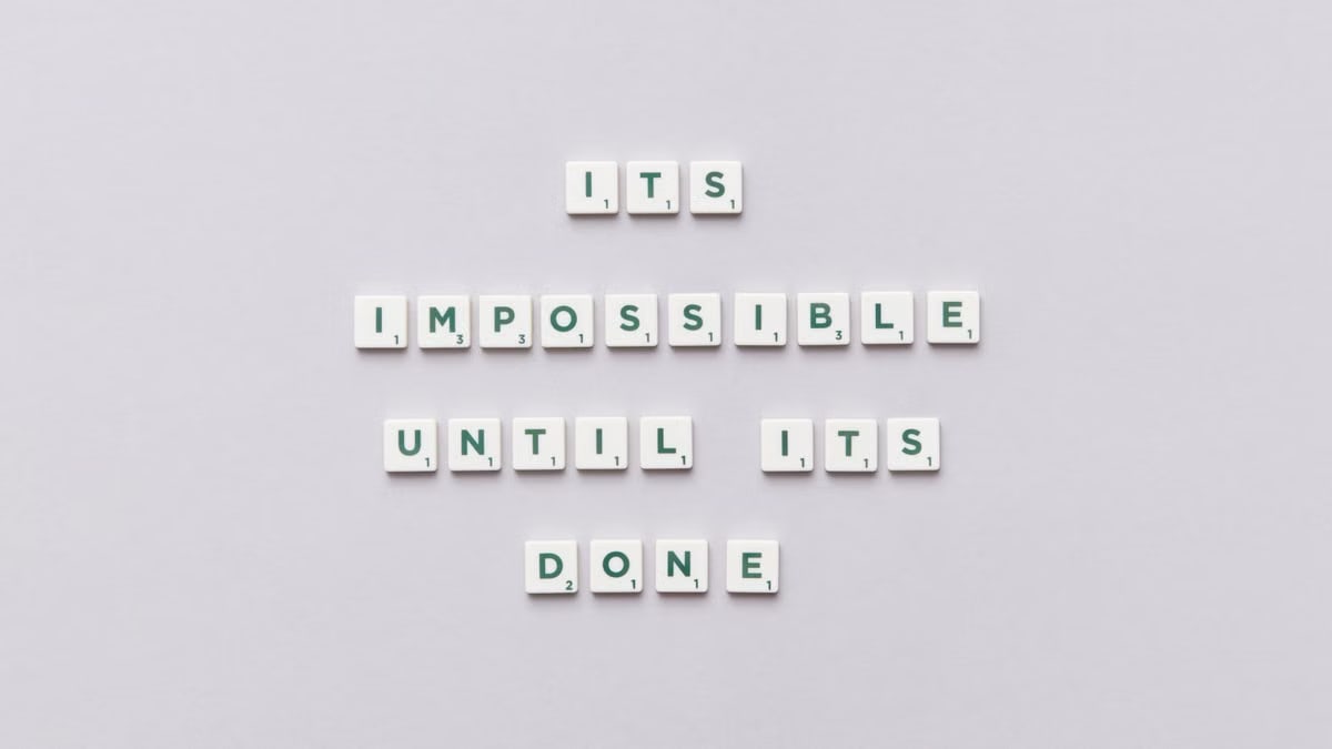 Motivational phrase 'It's impossible until it's done' arranged with Scrabble tiles on a gray background.